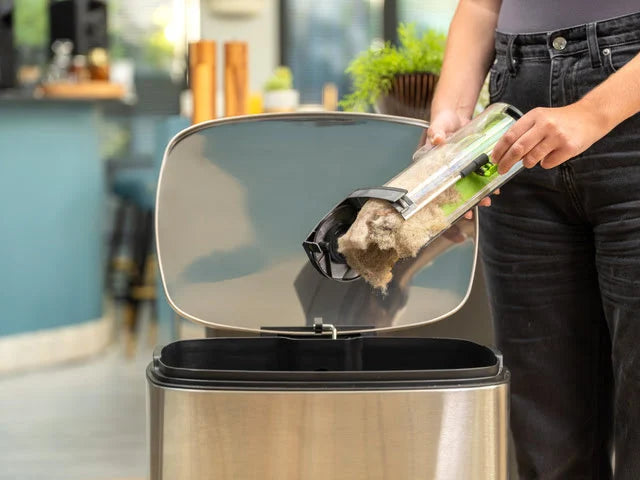 Lady emptying dirt out of the AirRAM 2 cordless vacuum cleaner easy-empty bin into a trash can.