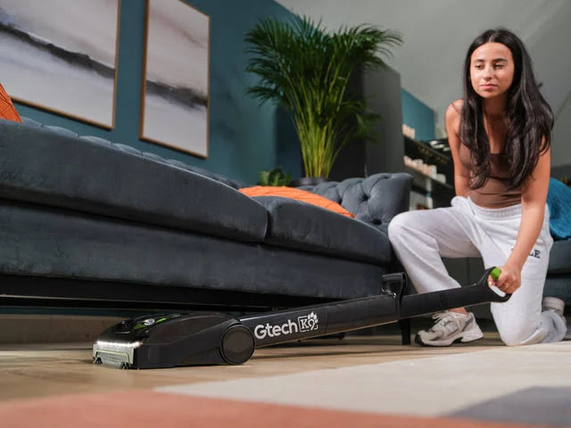 Woman using a Gtech AirAM 2 K9 Pet cordless vacuum cleaner in a living room.