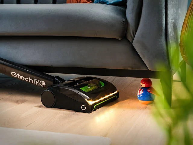 Gtech AirRAM 2 K9 Pet cordless vacuum cleaner with bright LED headlights vacuuming under sofa.