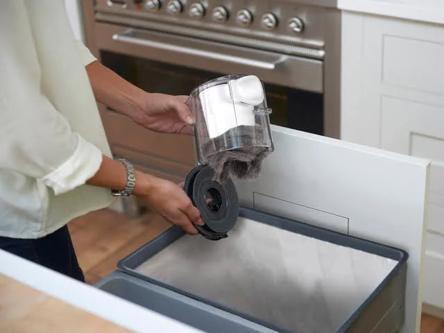 Lady emptying Multi Platinum cordless handheld vacuum easy-empty bin into trash can. 
