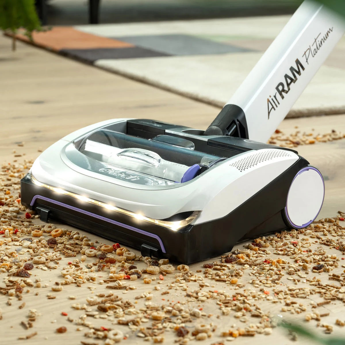 Close up of AirRAM Platinum Anti Hair Wrap cordless vacuum cleaner which is vacuuming cereal off wooden floor.