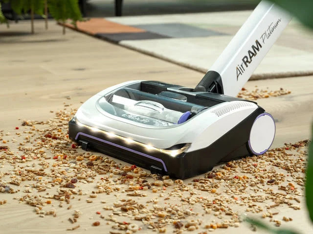 AIrRAM Platinum Anti Hair Wrap cordless vacuum picking up cereal from wooden floor.
