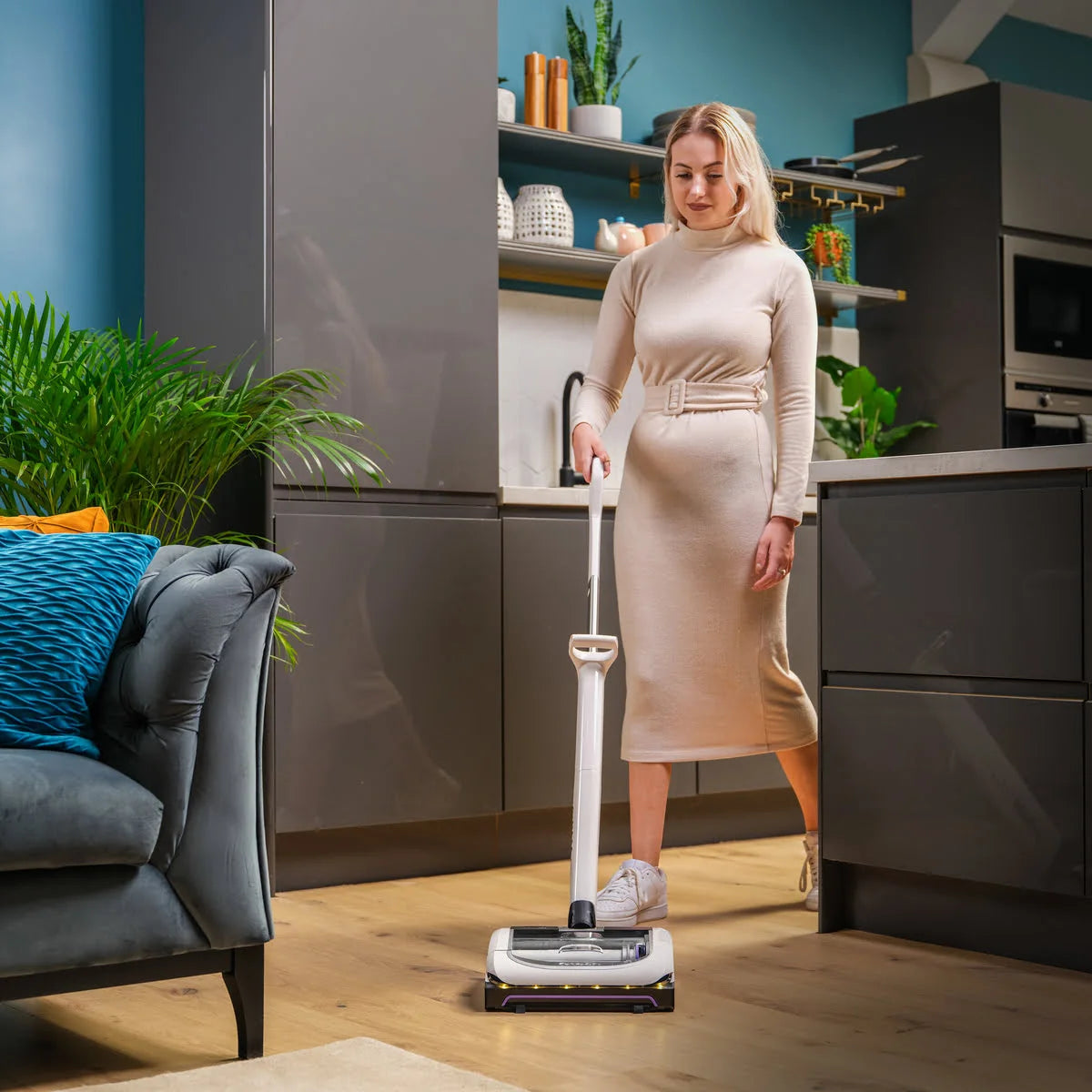Lady with long hair using the Gtech AirRAM Platinum Anti Hair Wrap cordless vacuum cleaner in living room.