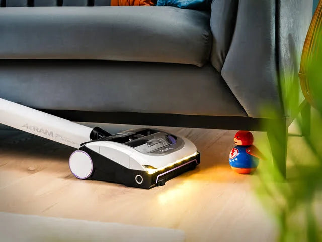 AirRAM Platinum Anti Hair Wrap cordless vacuum cleaner cleaning under a sofa with LED headlights on.