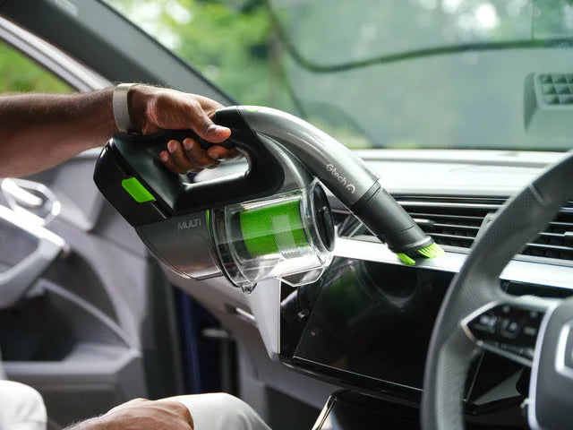 Man using LED headlight of Multi cordless handheld vacuum whilst vacuuming dirt from car dashboard.