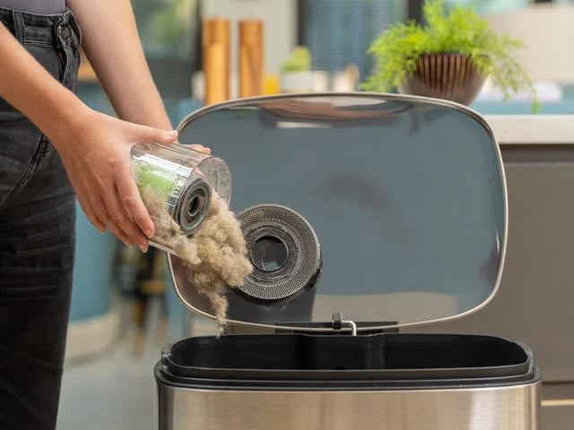 Lady emptying the Multi cordless handheld vacuum easy-empty in into trash can.