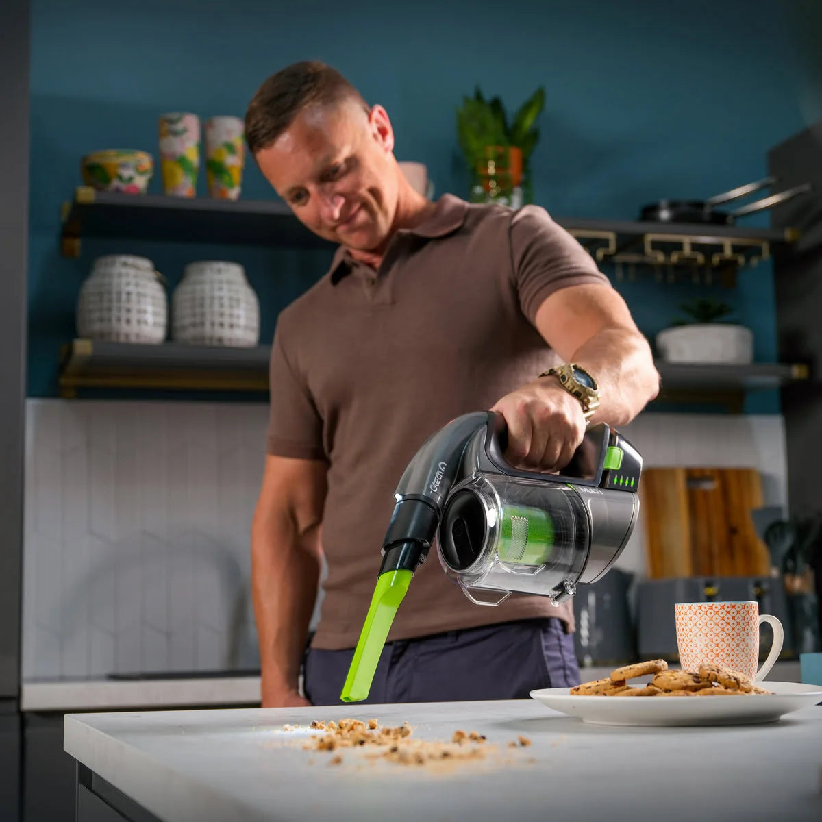 Man holding Multi cordless handheld vacuum with crevice tool attachment to pick up crumbs on kitchen counter.