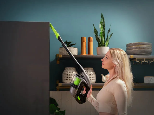 Lady using Multi handheld cordless vacuum with extension tube fitted to clean top of cupboard.