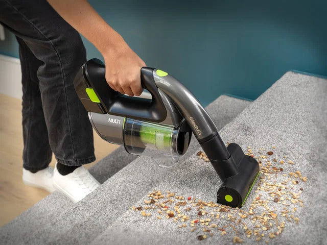 Lady using Multi handheld cordless vacuum to clean dirt and debris on carpeted stairs.