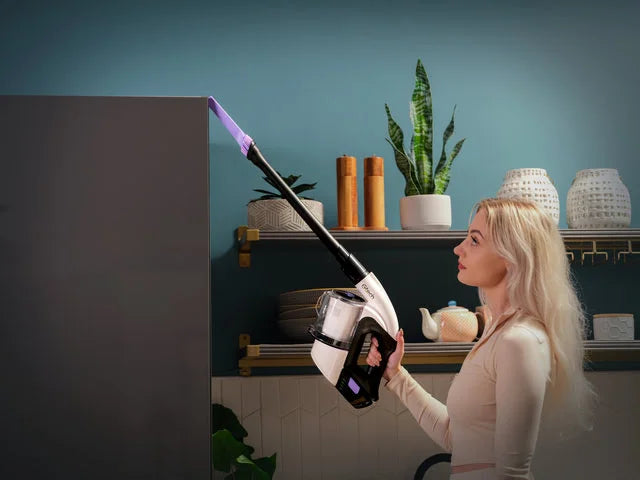 Woman using Multi Platinum handheld vacuum with crevice tool attachment to clean top of cupboard. 