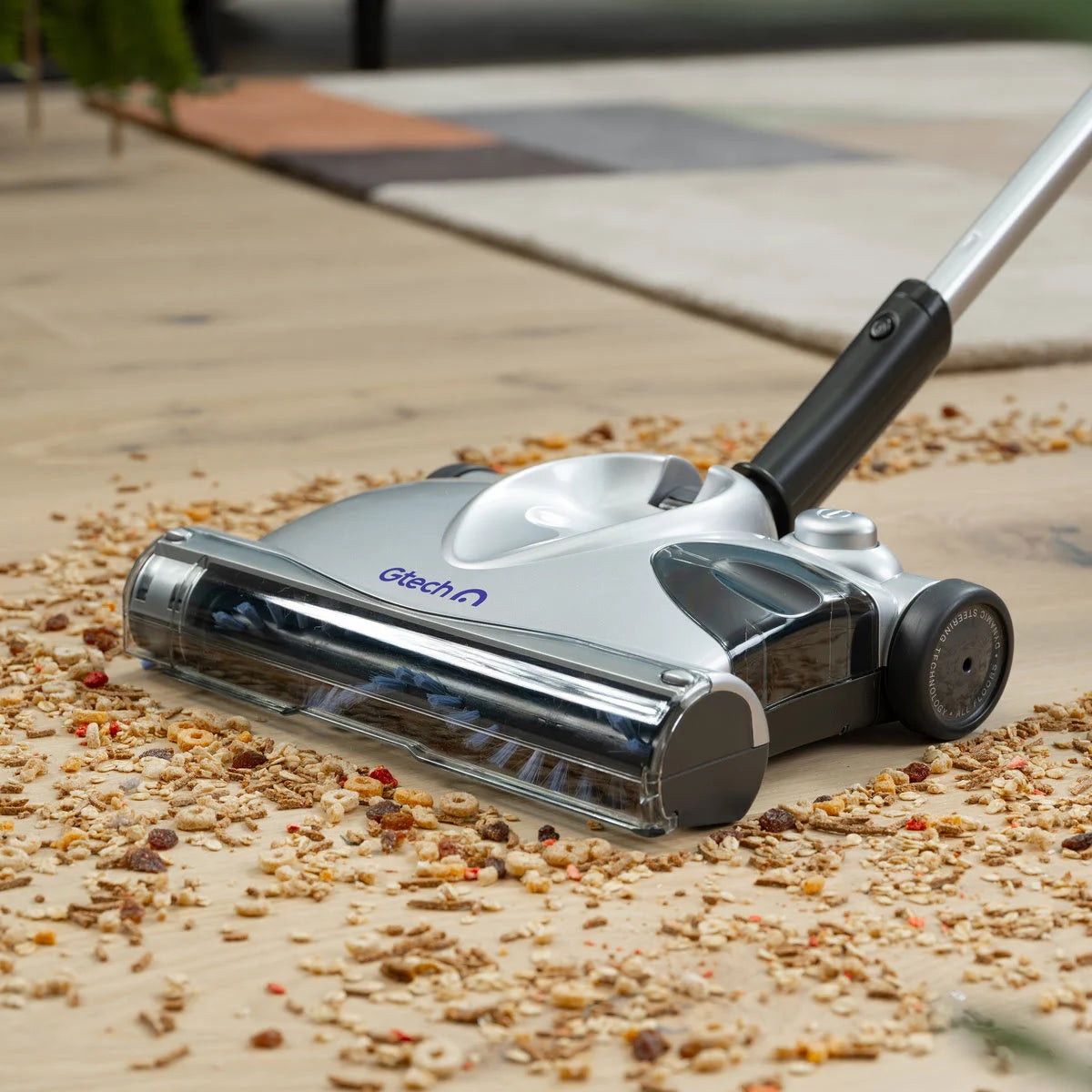 Close up of SWO2 cordless carpet sweeper picking up dirt and debris on wodden floor.