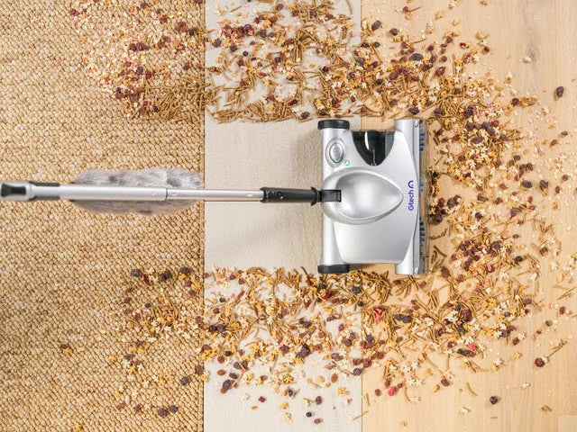 Overhead image of SW02 cordless carpet sweeper picking up debris on wooden floor with rug.