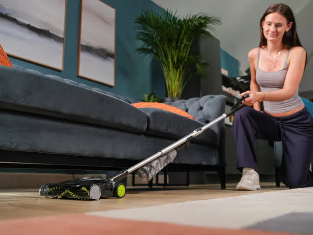 Lady using SW22 carpet sweeper under sofa with handle extended.